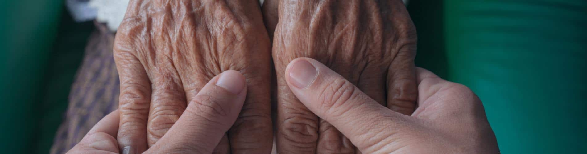 Manos de persona mayor sujetas por manos de persona joven dedos con arrugas artritis artrosis